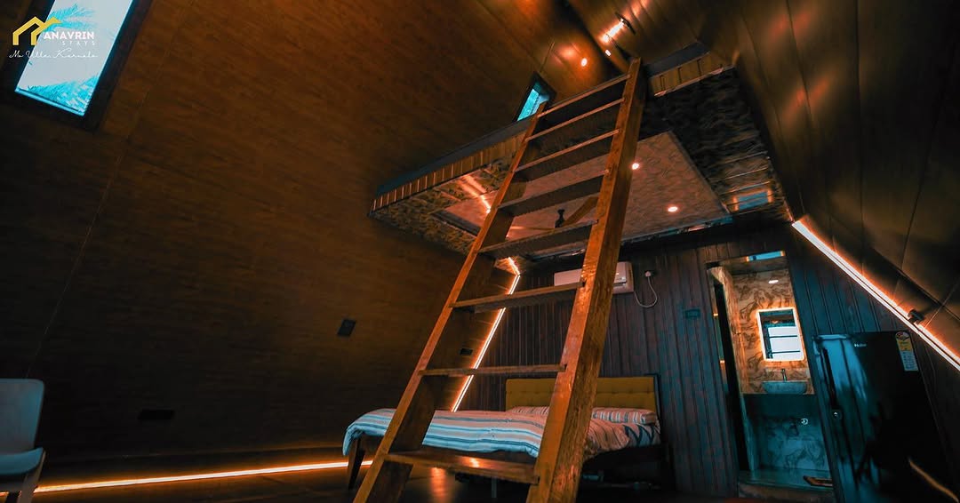 Inside an A-frame cabin at Mo Ville: wooden walls, a loft accessed by ladder, LED accent lighting, double bed below